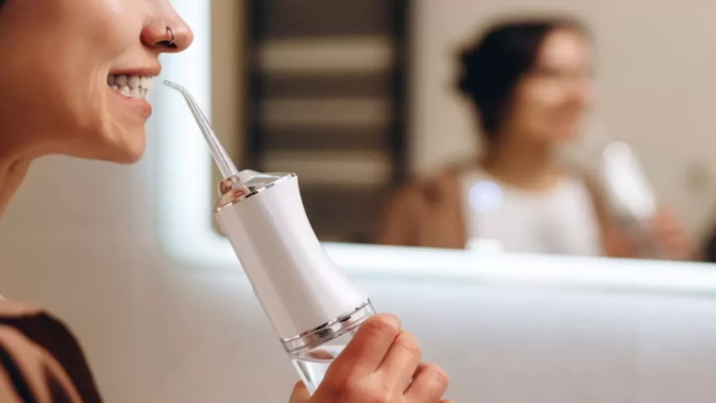 mulher limpando os dentes com irrigador dental